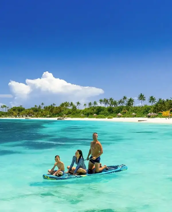 A family on a boat in a turquoise lagoon with a palm-fringed island behind