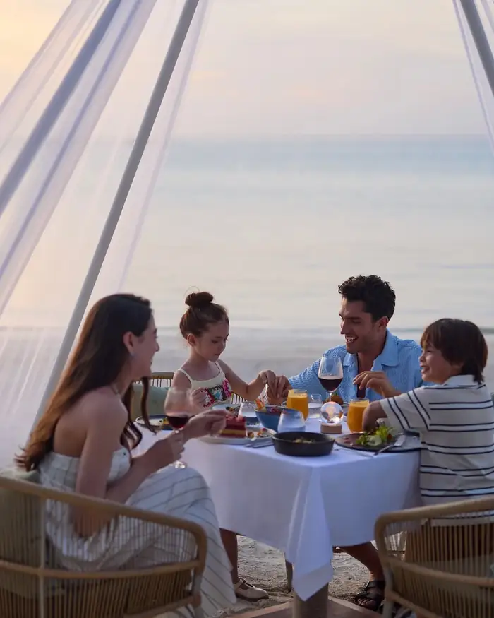 A family of four at dinner on the sand as the sky turns pink