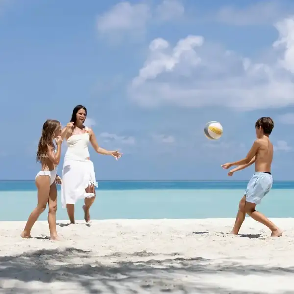A mother and two children playing with a ball on a white Maldives beach