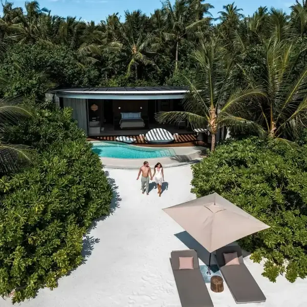 A couple walking towards a private pool villa among tropical gardens, seen from above