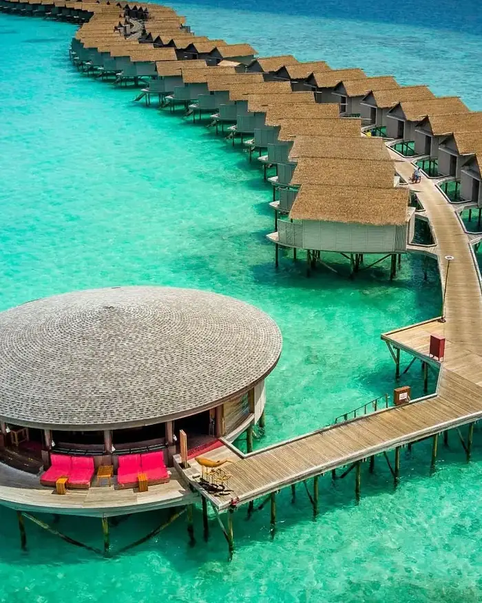 A row of overwater villas curving away above a turquoise lagoon