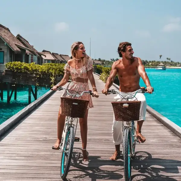 A couple cycling along a wooden jetty past overwater villas