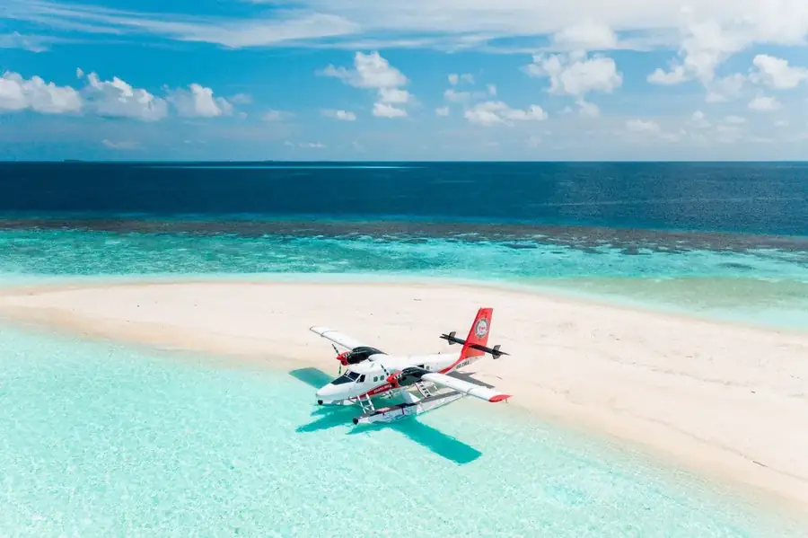 A seaplane resting on a white sandbank ringed by shallow turquoise water