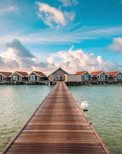 Three overwater villas on a curving boardwalk above a bright turquoise reef