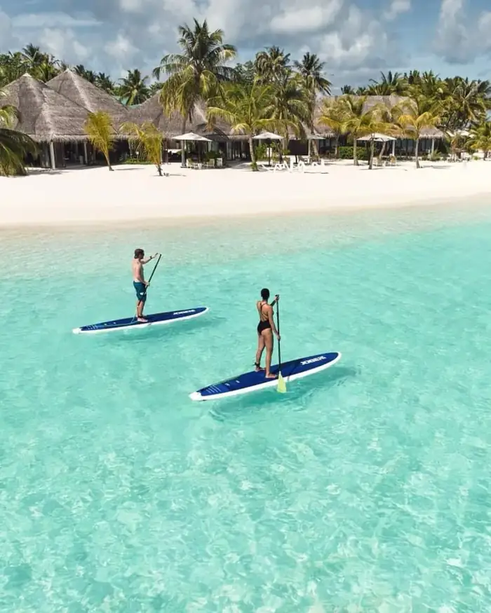 Thatched beach villas and loungers behind a white beach and a clear turquoise lagoon