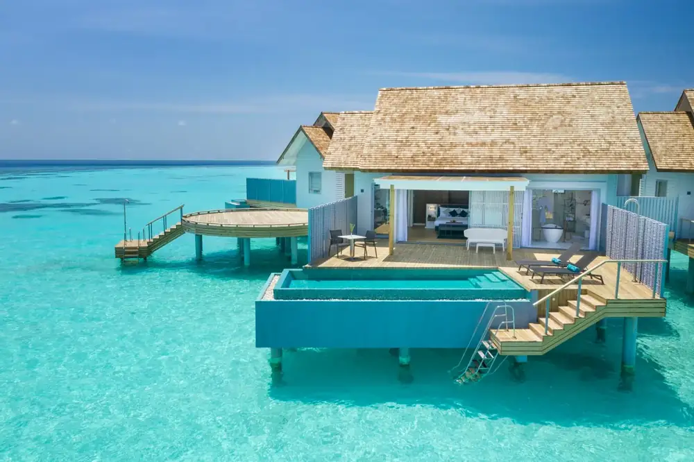 An overwater villa on stilts above a turquoise lagoon with a private pool and steps into the water