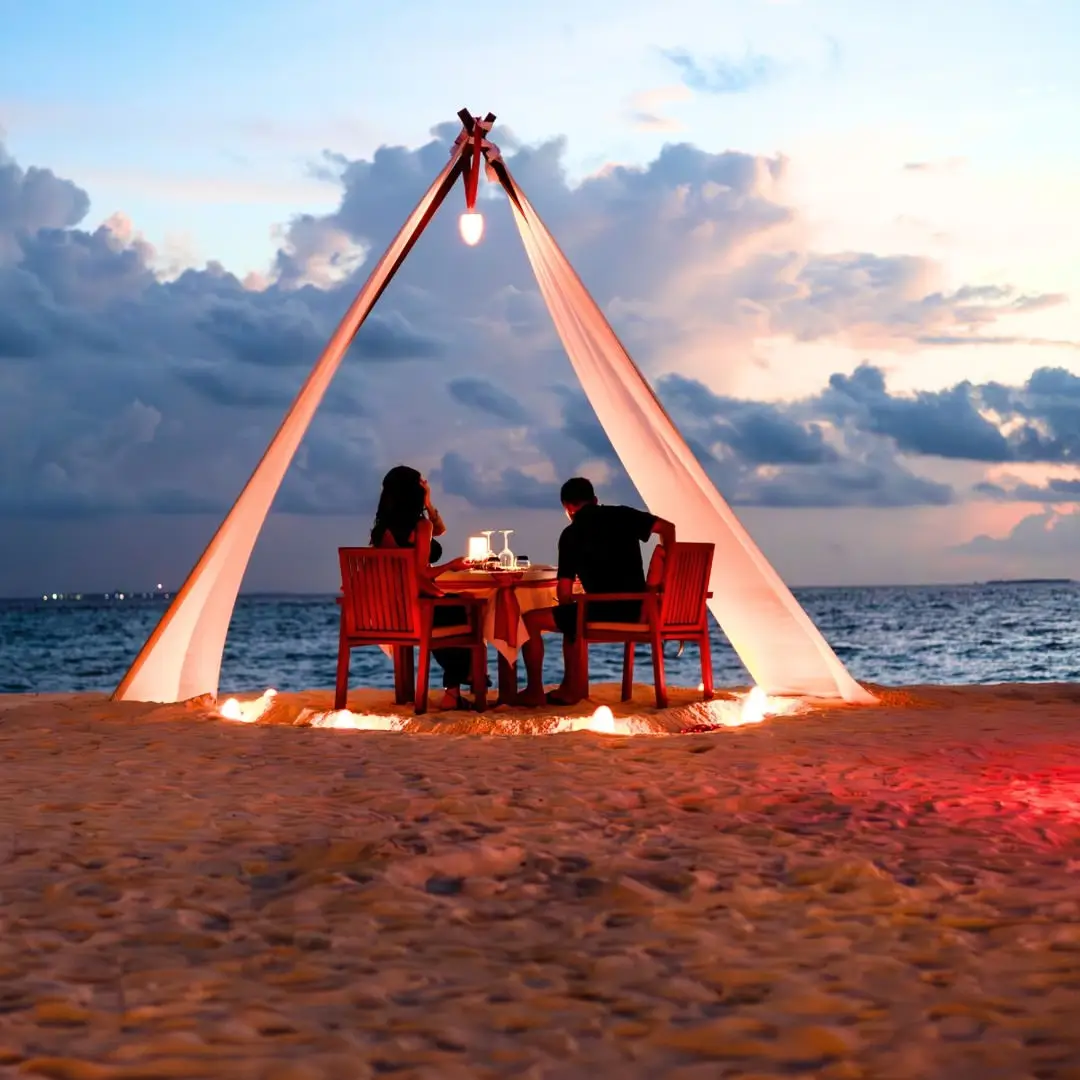 A private candlelit beach dinner set up for two on the sand at sunset in the Maldives