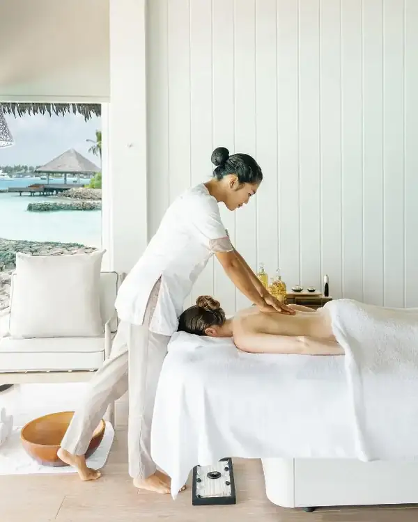 A guest receiving a massage in a bright spa room with sea views